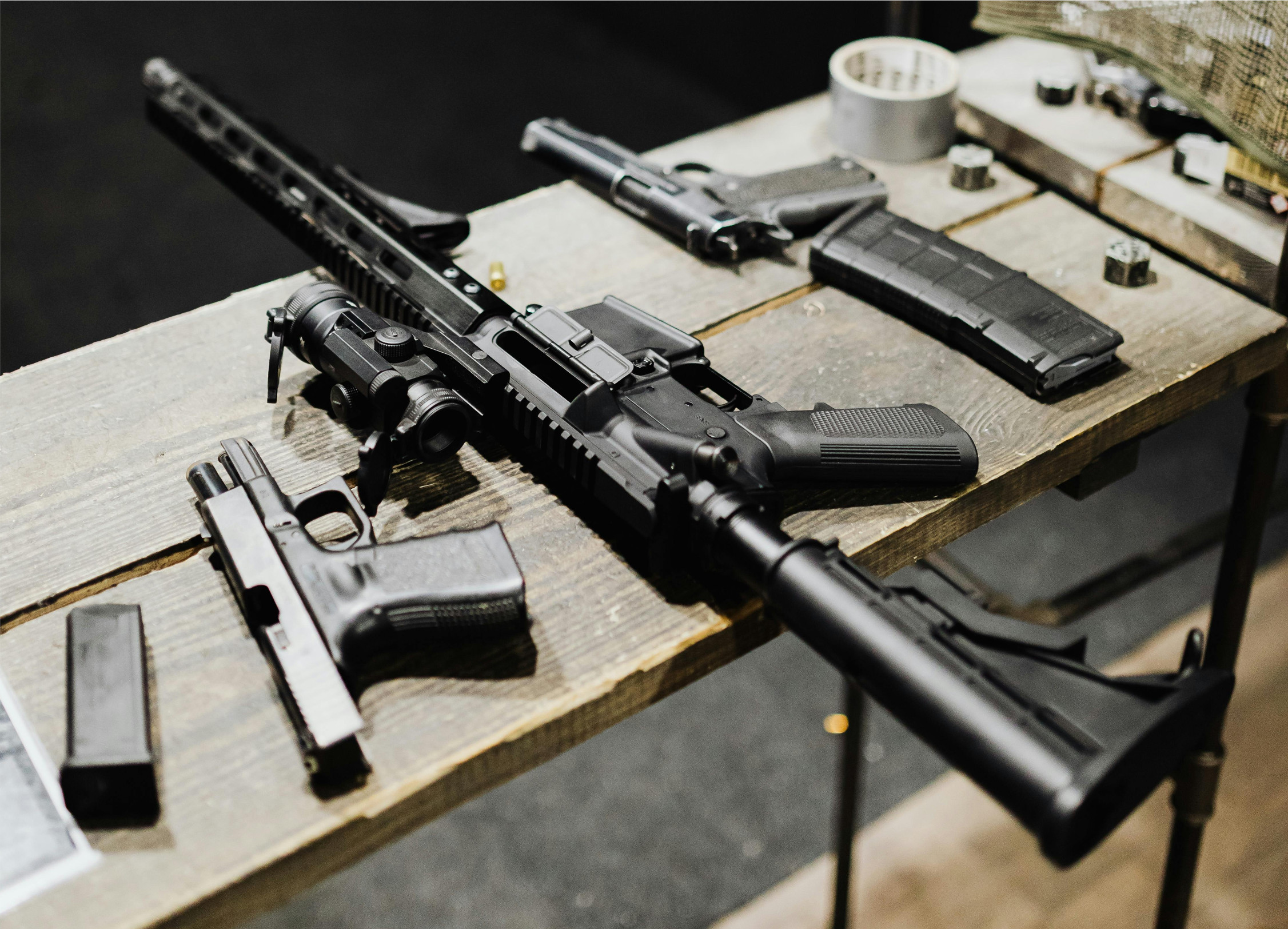 Two handguns, a rifle, and associated magazines sitting on a wooden workbench.